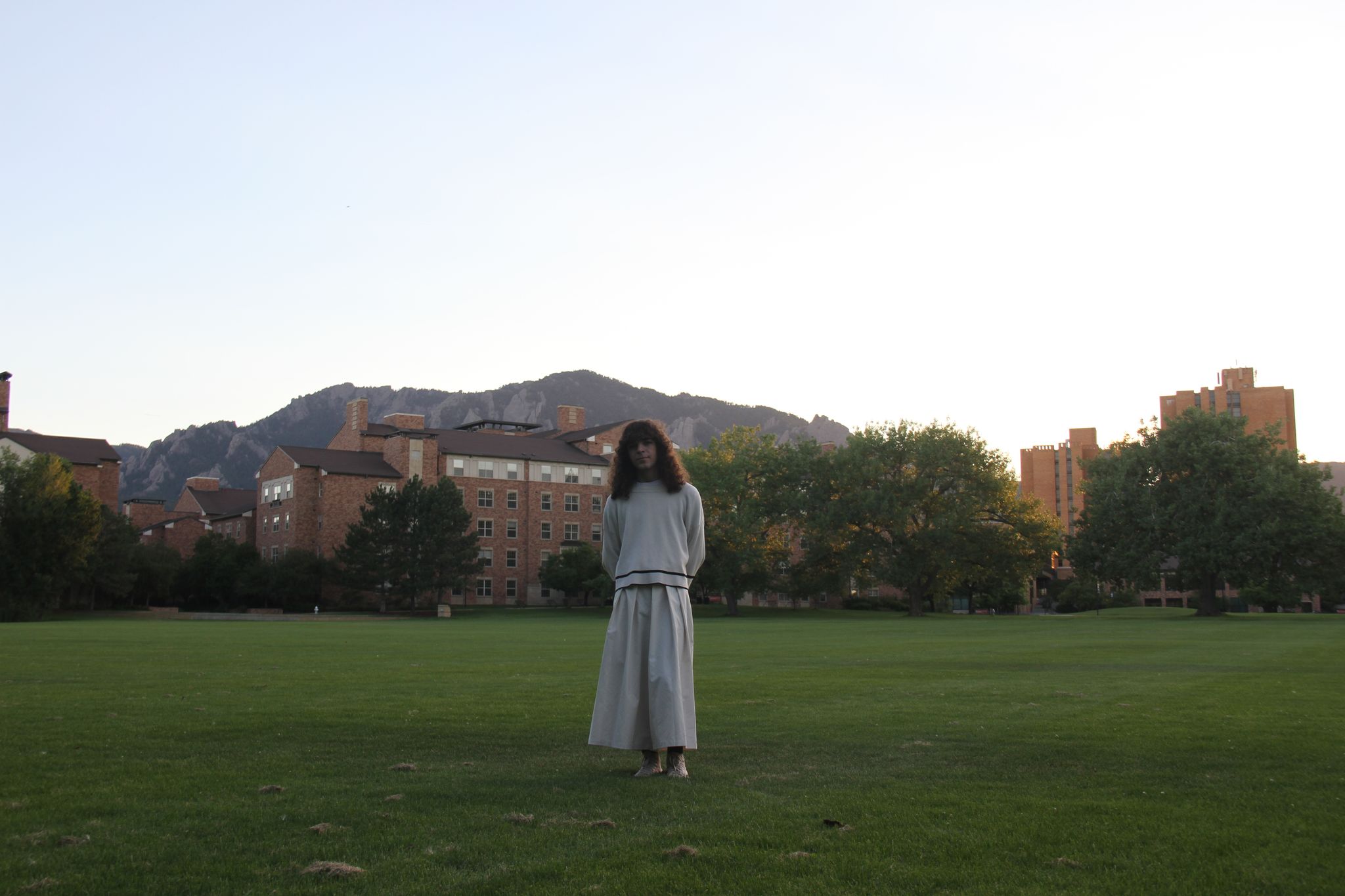 someone standing in a grassy field on the CU Boulder campus, the Flatirons behind them