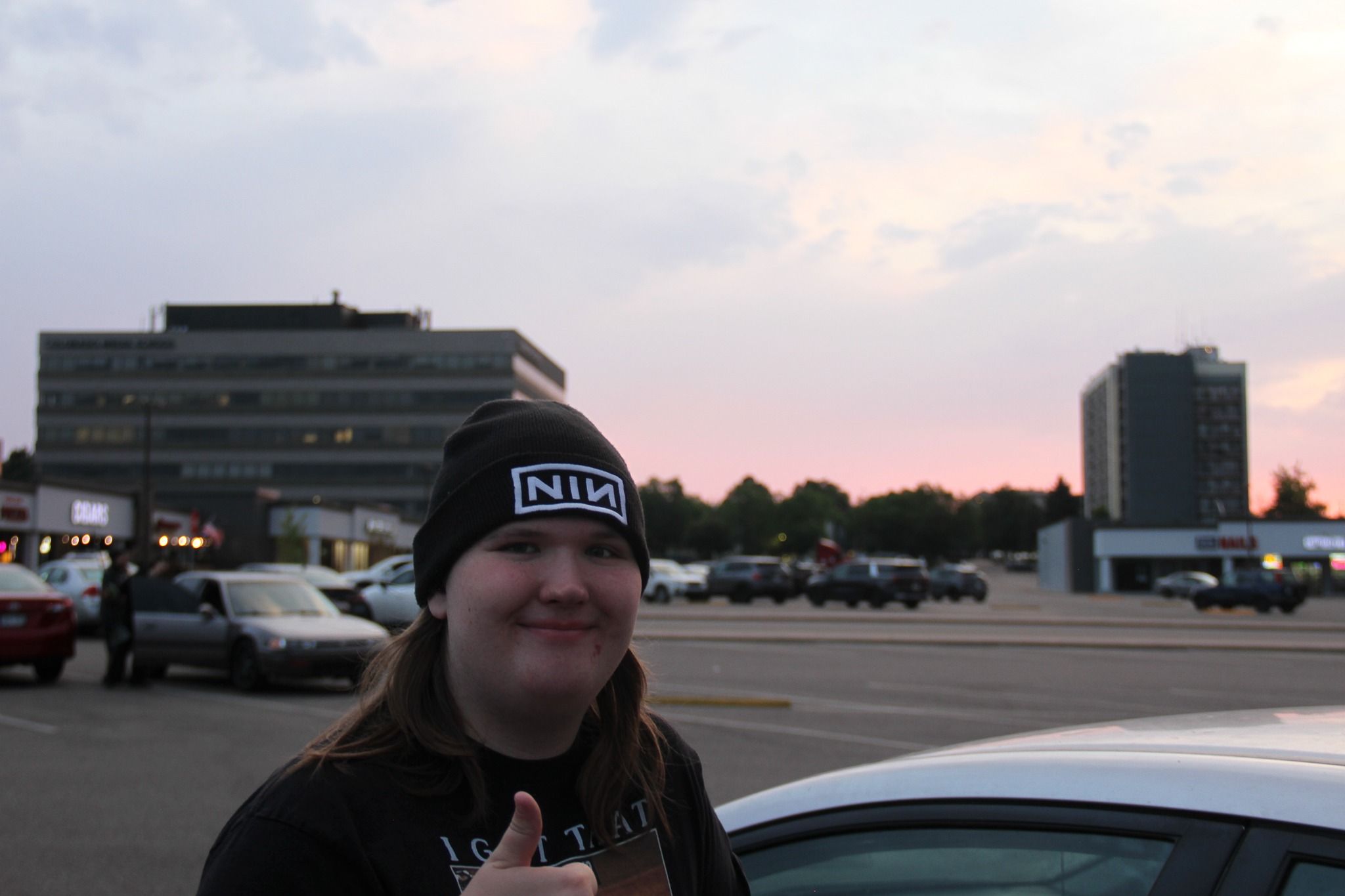 a friend in a Nine Inch Nails beanie giving a thumbs up in a parking lot at dusk