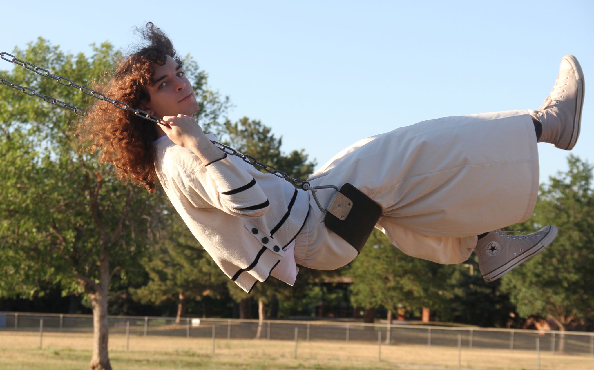 someone mid-swing on a playground swing, leaning way back with curly hair flying